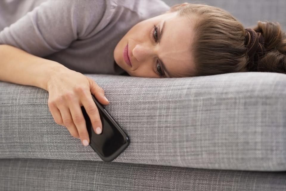 A woman laying on sofa holding phone.
