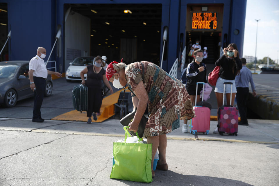 Travellers wearing face masks to protect against the spread of coronavirus, disembark from a ferry at the port of Piraeus, near Athens, Thursday, Aug. 20, 2020. Authorities in Greece are using free on-the-spot tests for ferry passengers and nightlife curfews on popular islands to stem a resurgence of the coronavirus after the country managed to dodge the worst of the pandemic. The number of confirmed virus cases and deaths in Greece remains lower than in many other European countries. (AP Photo/Thanassis Stavrakis)