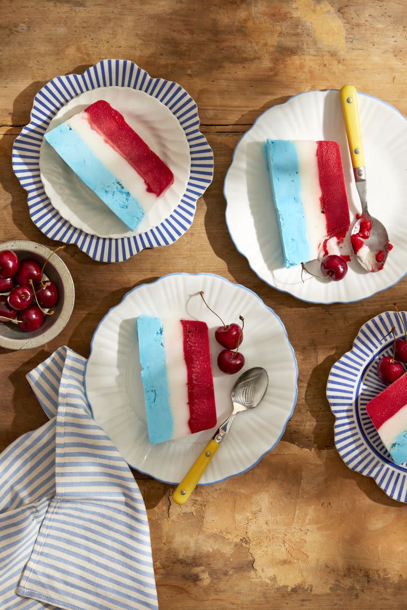 red, white blue striped sorbet loaf on white plates with blue details and yellow handled spoons, garnished with fresh cherries