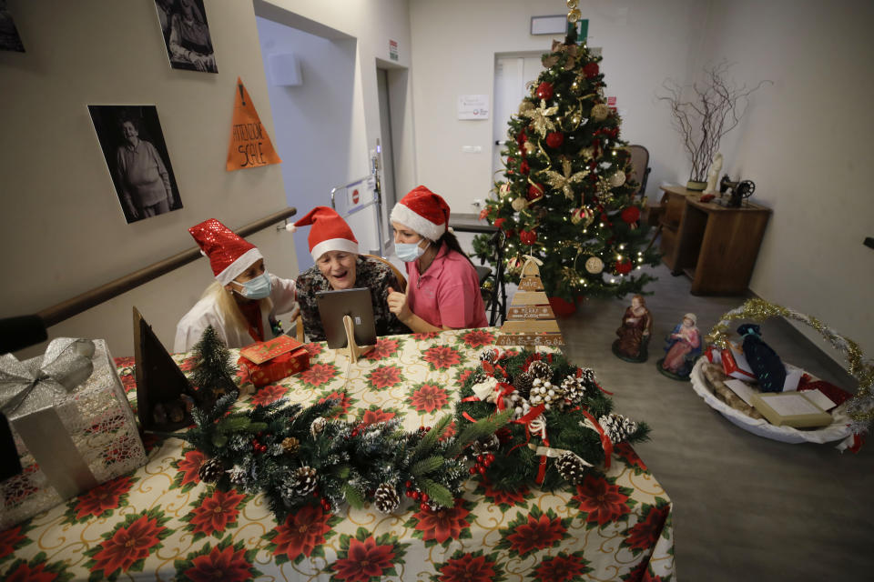 Caterina Bertocchi, is flanked by health care worker Michela Valle, right, and director Maria Giulia Madaschi, as she talks a video call with Irene Schiavone, a donor unrelated to her, who bought and sent her a Christmas present through an organization dubbed "Santa's Grandchildren", at the Martino Zanchi nursing home in Alzano Lombardo, one of the area that most suffered the first wave of COVID-19, in northern Italy, Saturday, Dec. 19, 2020. (AP Photo/Luca Bruno)