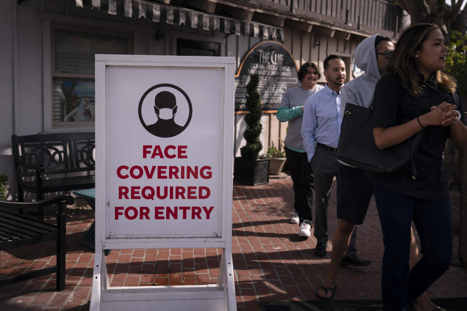 People walk past a sign requesting customers to wear masks in Laguna Beach, Calif., Monday, May 17, 2021. California won't lift its mask requirement until June 15 to give the public and businesses time to prepare and ensure cases stay low, state Health Director Mark Ghaly said Monday. (AP Photo/Jae C. Hong)