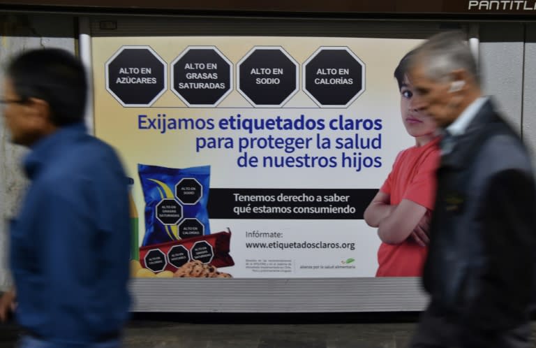 Unas personas caminan frente a un cartel de etiquetado nutricional de advertencia en alimentos en Ciudad de México el 1 de octubre de 2019 (Rodrigo Arangua)