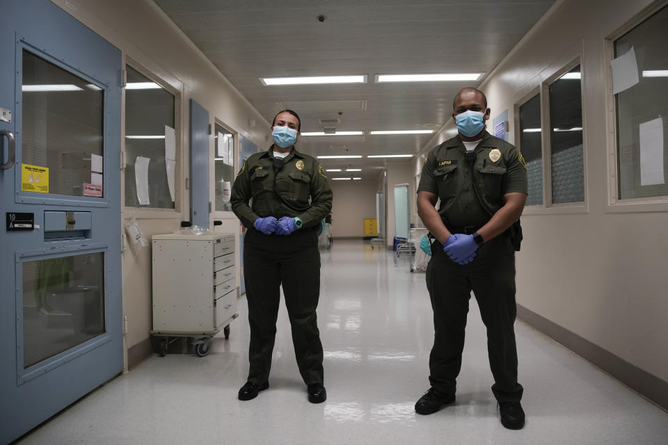 In this April 16, 2020, photo Sonia Munoz, left, and Christopher Lumpkin, custody assistants, poses for a picture at the hospital ward of the Twin Towers jail in Los Angeles. Across the country first responders who've fallen ill from COVID-19, recovered have begun the harrowing experience of returning to jobs that put them back on the front lines of America's fight against the novel coronavirus. (AP Photo/Chris Carlson)