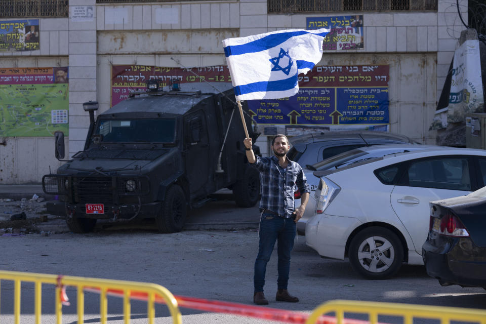 A Jewish settler waves the Israeli flag as protesters heckle activist on a "solidarity tour" of the embattled West Bank city of Hebron, Friday, Dec. 2, 2022. Israeli peace activists toured the occupied West Bank's largest city Friday in a show of solidarity with Palestinians, amid chants of "shame, shame" from ultra-nationalist hecklers. The encounter in the center of Hebron signaled the widening rift among Israelis over the nature of their society and Israel's open-ended military rule over the Palestinians, now in its 56th year. (AP Photo/ Maya Alleruzzo)