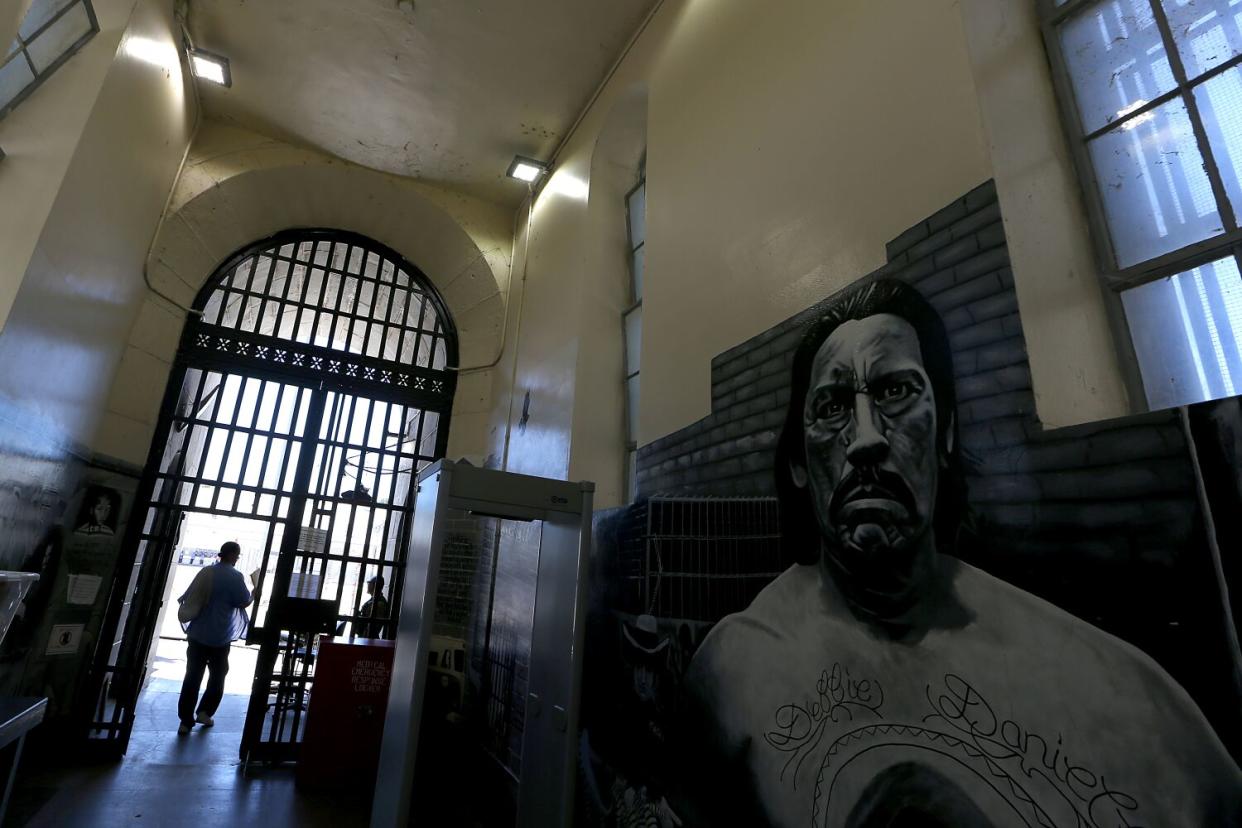 A person walking through a barred doorway near a large black-and-white mural of a man