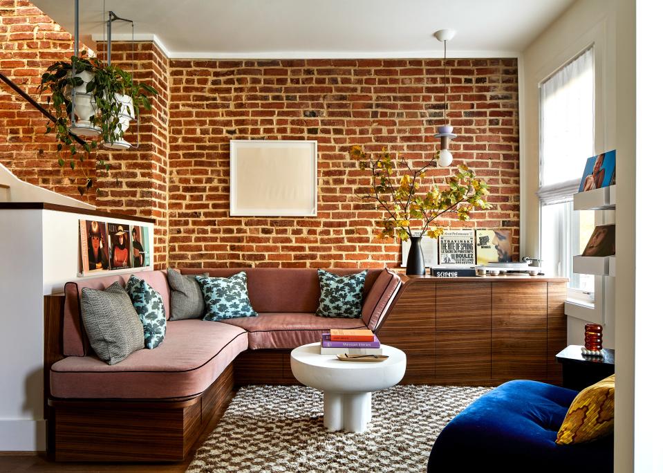 A brick wall backdrops the living area, where a riot of color spills forth in the way of large photographs, a Junit pendant by Schneid Studio, and pillows dressed in Dedar’s whimsical Be Bop A Lula fabric. Zoë softened the built-in walnut sofa, custom-made by Fajen & Brown, with Looney & Sons cushions outfitted in Mokum’s Alpaca velvet upholstery and Samuel & Sons’s Swiss velvet piping. A bone white Crown table by 101 Copenhagen takes center stage. The couple’s prized Marantz turntable sits atop the custom storage unit. “The place is like a ’70s-era conversation pit, but on a smaller scale. Seeing it come to life was amazing,” says one husband.