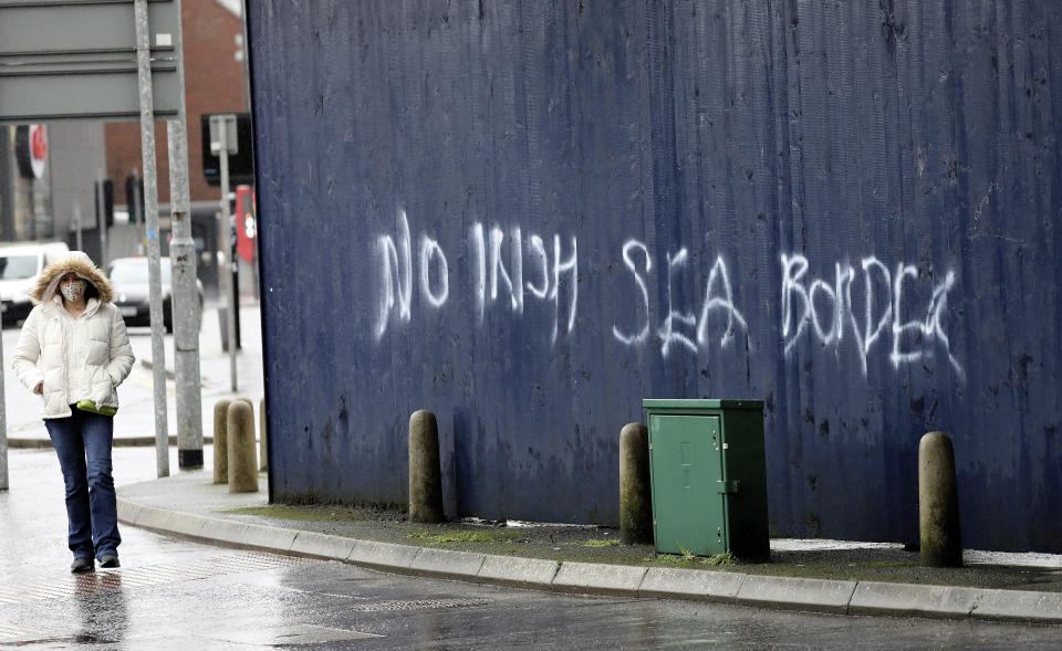 A woman walks past past graffiti with the words 'No Irish Sea Border' in Belfast city centre, Northern Ireland, Wednesday, Feb. 3, 2021. Politicians from Britain, Northern Ireland and the European Union are meeting to defuse post-Brexit trade tensions that have shaken Northern Ireland’s delicate political balance. British Cabinet minister Michael Gove, European Commission Vice President Maros Sefcovic and the leaders of Northern Ireland’s Catholic-Protestant power-sharing government will hold a video conference to discuss problems that have erupted barely a month after the U.K. made an economic split from the 27-nation EU. (AP Photo/Peter Morrison)