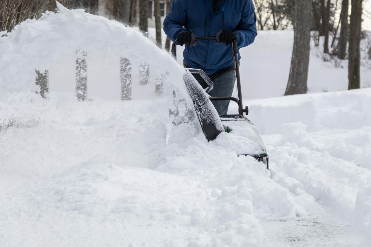 Snow blower in action clearing a residential driveway after snow storm.  Snow removal, winter snow storm, weather concept.