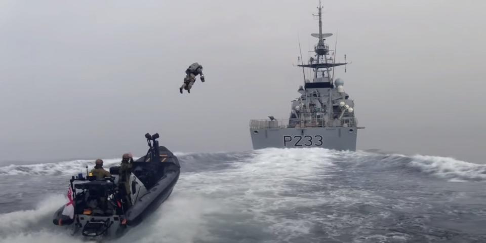 A Royal Marine in a jetpack launches from a fast boat to board a Royal Navy ship.