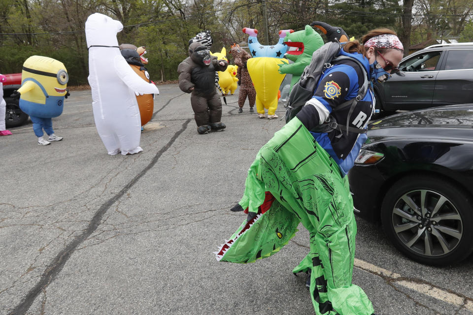 In this Monday, May 11, 2020 photo, Keely Crimando, a member of the T-Rex Walking Club, puts on her costume in Ferndale, Mich. The group takes its unannounced strolls through neighborhoods on a quest to bring smiles to the faces of kids, and a few adults, while under Michigan's stay-at-home order because of the COVID-19 pandemic. (AP Photo/Carlos Osorio)