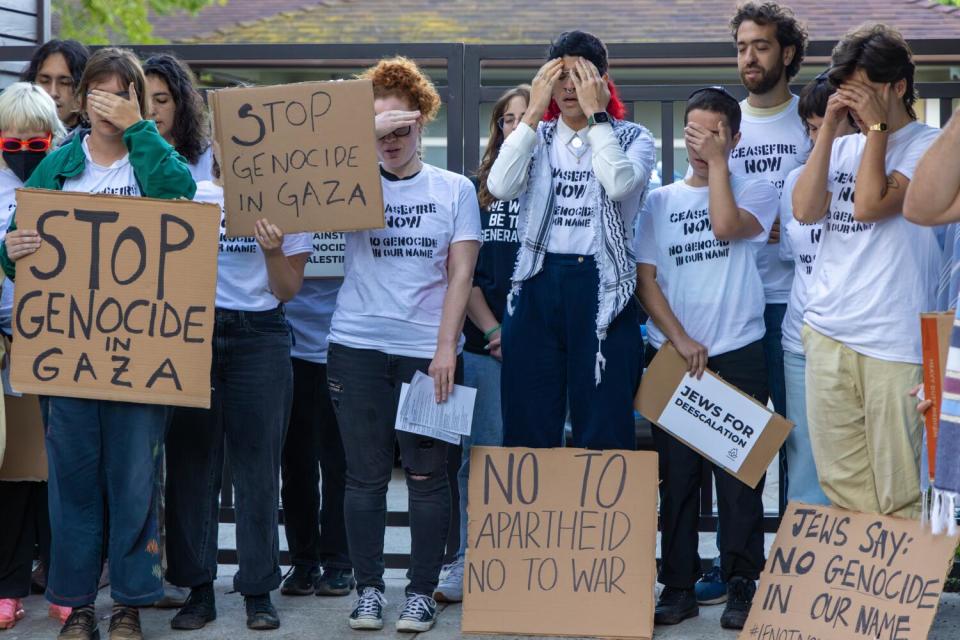 Demonstrators, some holding cardboard signs, cover their eyes.