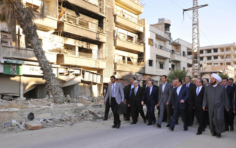 FILE - In this Sept. 12, 2016, file photo, released by the Syrian official news agency SANA, Syrian President Bashar Assad, center, walks on a street with officials after performing the morning Eid al-Adha prayers in Daraya, a blockaded Damascus suburb, Syria. Assad has snapped up a prize from world powers that have been maneuvering in his country’s multifront wars. Without firing a shot, his forces are returning to towns and villages in northeastern Syria where they haven’t set foot for years. (SANA via AP, File)