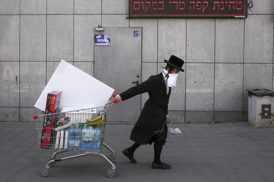 FILE - In this April 3, 2020, file photo, an ultra-Orthodox Jew wears an improvised protective face mask as he pulls a supermarket cart on a mainly deserted street because of the government's measures to help stop the spread of the coronavirus, in Bnei Brak, a suburb of Tel Aviv, Israel. That's the harsh truth facing workers laid off around the world, from software companies in Israel to restaurants in Thailand and car factories in France, whose livelihoods fell victim to a virus-driven recession that's accelerating decline in struggling industries and upheaval across the global workforce. (AP Photo/Oded Balilty, File)