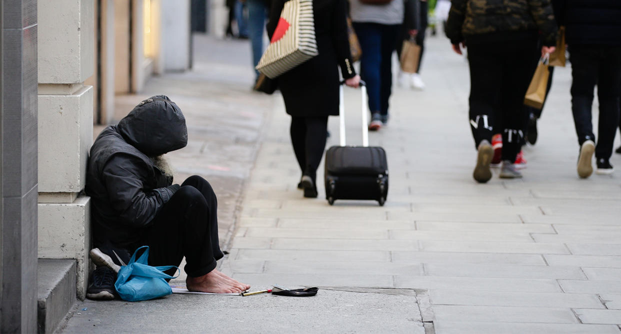 A homeless person sitting on the street next to passers-by in winter. (Getty Images)