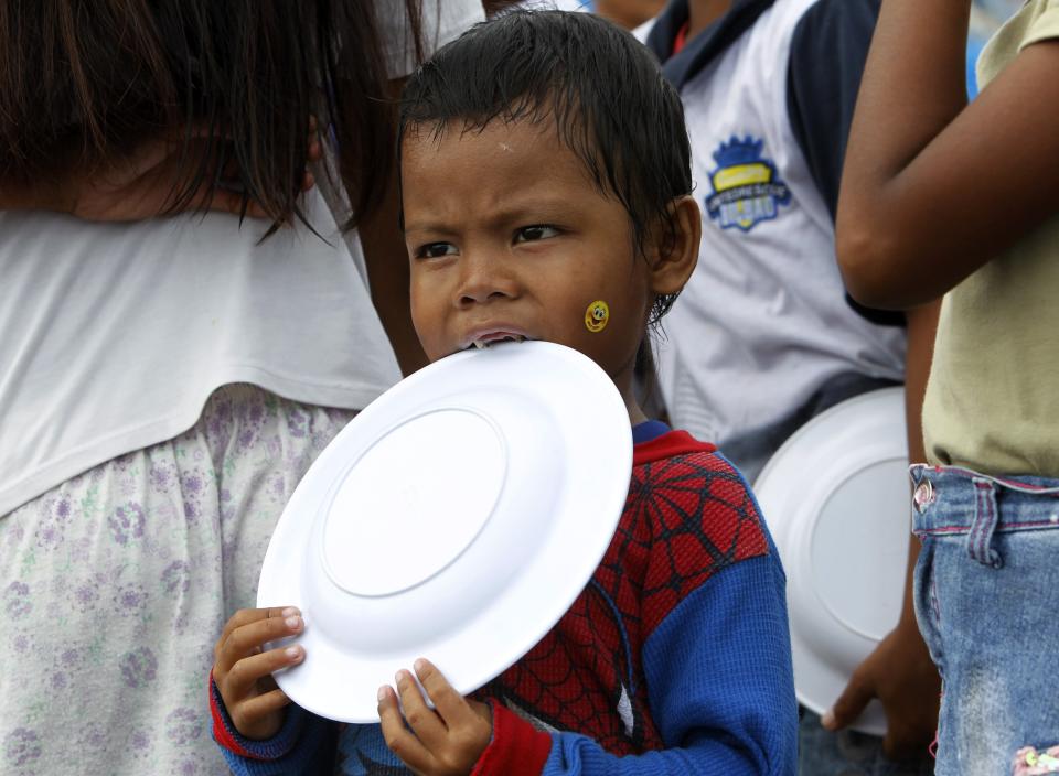 A boy bites his empty plate while queuing for a free meal during Christmas celebrations at the town of Bislig, Tanauan in Leyte province, central Philippines December 24, 2013, a month after Typhoon Haiyan battered central Philippines. Super typhoon Haiyan reduced almost everything in its path to rubble when it swept ashore in the central Philippines on November 8, killing at least 6,069 people, leaving 1,779 missing and 4 million either homeless or with damaged homes. REUTERS/Romeo Ranoco (PHILIPPINES - Tags: DISASTER SOCIETY)