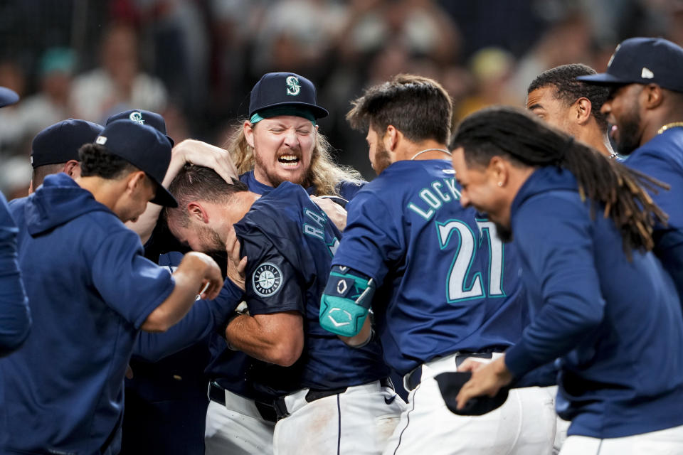 Seattle Mariners' Cal Raleigh is mobbed by teammates, including relief pitcher Ryne Stanek, facing, and Tyler Locklear (27) after hitting a game-winning grand slam against the Chicago White Sox in a baseball game Monday, June 10, 2024, in Seattle. The Mariners won 8-4. (AP Photo/Lindsey Wasson)