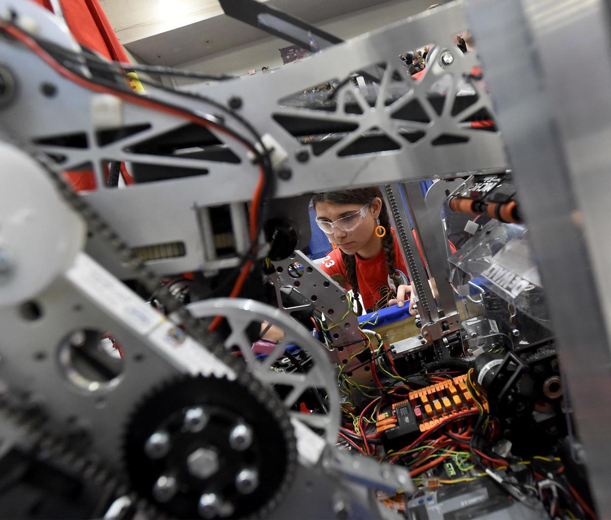 Drive team technician Olivia Szczepanik takes a close look at parts of the Bedford Express FRC Team #1023 robot before going into competition on the DTE Foundation Field at the FIRST in Michigan State Championship 2024 at Saginaw Valley State University April 5, 2024. Notice the notes (orange rings) she is wearing as a fellow teammate made them on a 3D printer.