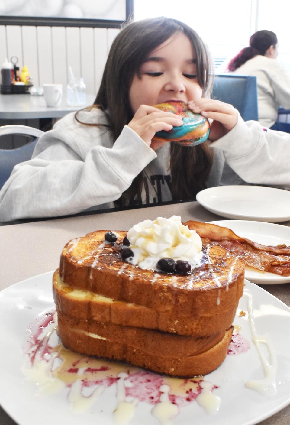 Aubrey Bigelow eats a bagel at Twisted Griddle on Wednesday Sept. 27, 2023. In the foreground is a plate of Blueberry Cheesecake French Toast.