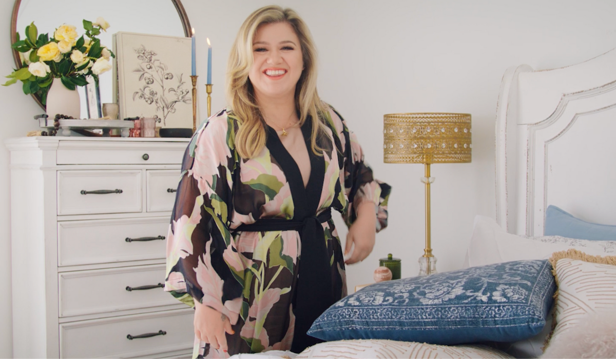 Kelly Clarkson standing next to a bed in a still from her Kelly Clarkson Home Wayfair product page video