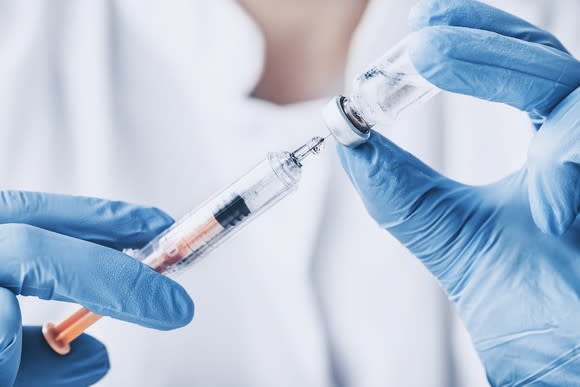 Gloved hands holding syringe and vaccine bottle