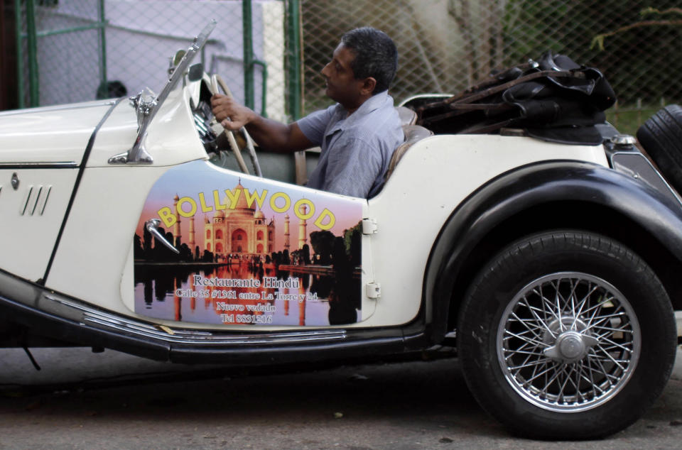In this June 9, 2012 photo, Cedric Fernando parks his 1955 GM car, with his door covered by advertising for his wife's restaurant, "Bollywood," at his home in Havana. For decades, Communist-run Cuba has essentially been free of commercial advertising. But it's a knotty problem for thousands of budding entrepreneurs who have embraced President Raul Castro's push for limited free-market reform. So they're turning to guerrilla marketing. (AP Photo/Franklin Reyes)