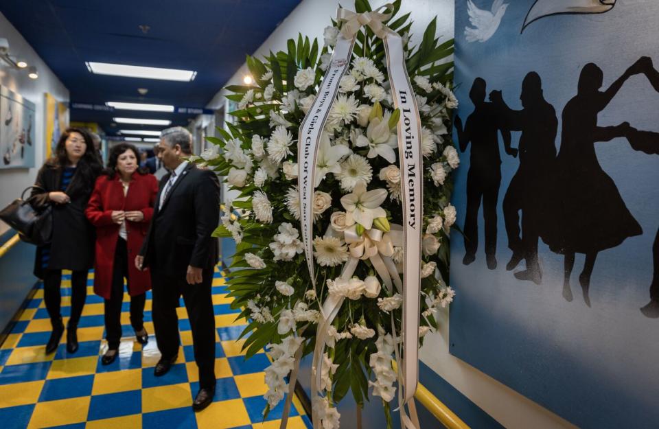 A woman in a red jacket is flanked by another woman and a man near a display of white flowers indoors