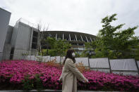 A woman wearing a protective mask to help curb the spread of the coronavirus walks near the Japan National Stadium, where opening ceremony and many other events are planned for postponed Tokyo 2020 Olympics Tuesday, April 6, 2021, in Tokyo. Many preparations are still up in the air as organizers try to figure out how to hold the postponed games in the middle of a pandemic. (AP Photo/Eugene Hoshiko)