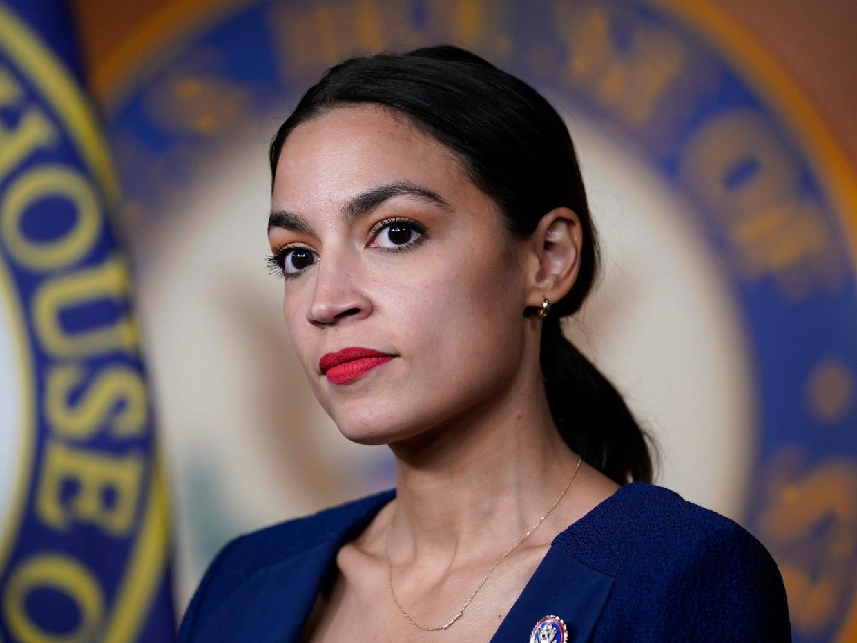 New York Congresswoman Alexandria Ocasio-Cortez in a blue blazer in front of a House of Representatives seal