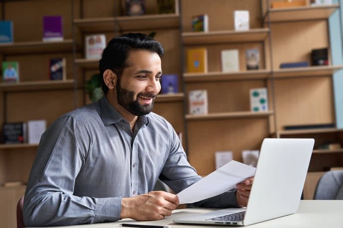 A smiling person on a video call with their laptop in a home office.