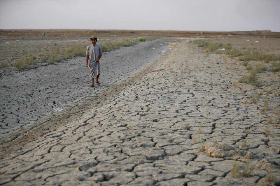 A fisherman walks across a dry patch of land in the marshes of southern Iraq which has suffered dire consequences from back to back drought and rising salinity levels, in Dhi Qar province, Iraq, Friday Sept. 2, 2022. (AP Photo/Anmar Khalil)