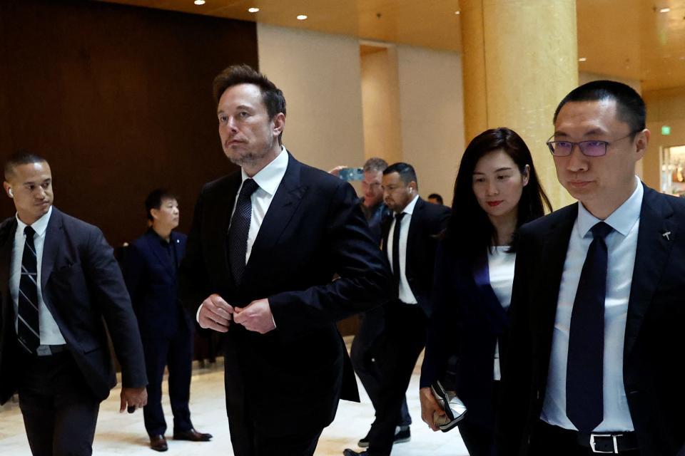 Elon Musk walks next to Tesla's Senior Vice President Tom Zhu and Vice President Grace Tao as he leaves a hotel in Beijing