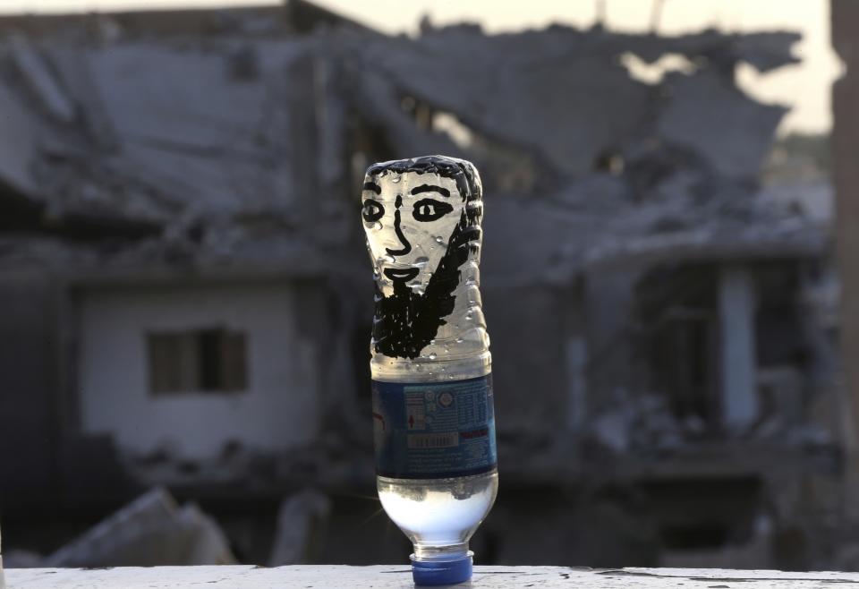 <p>Eine Wasserflasche mit dem aufgemalten Antlitz eines IS-Terroristen steht in einem umkämpften Gebiet der Stadt Rakka. (Bild: AP Photo/Hussein Malla) </p>