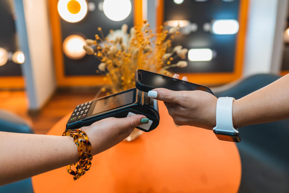 Side view of crop hand of female customer standing next to counter and paying with smartphone using NFC technology