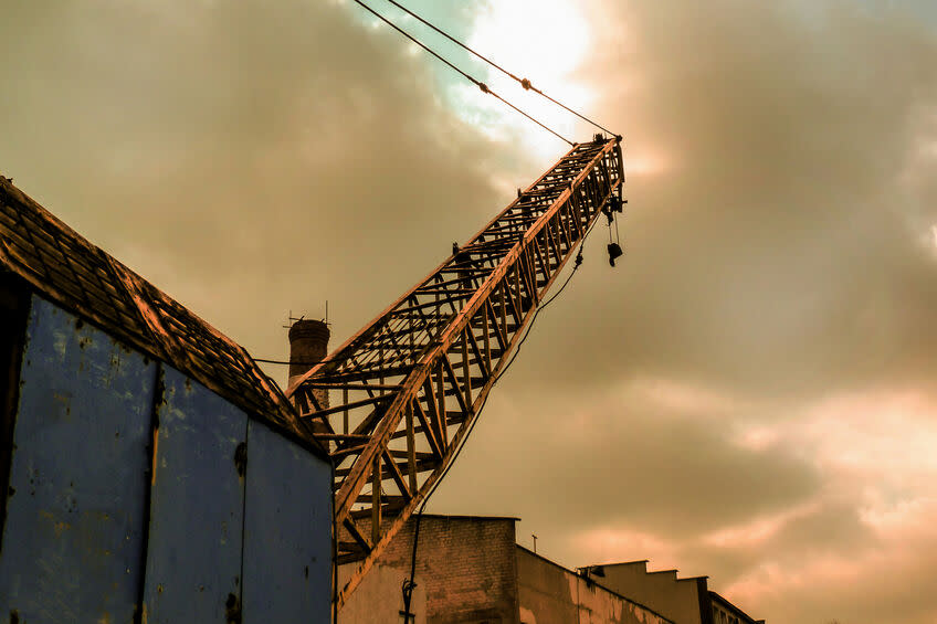 A large abandoned crane stands new land under large clouds.