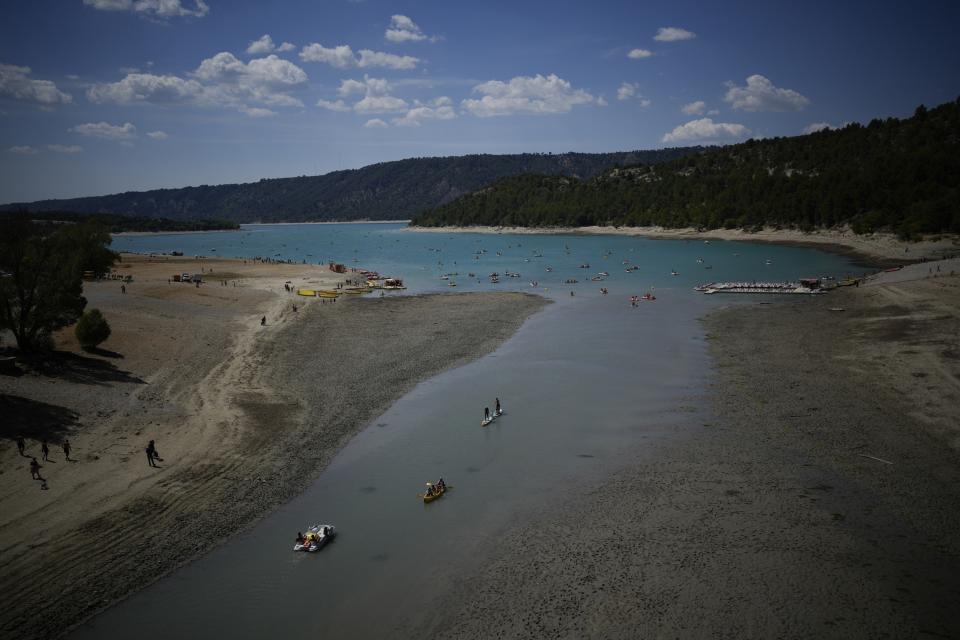 People enjoy water activities on the Lake of Sainte-Croix, southern France, as the water level continued to decline, Tuesday, Aug. 9, 2022. Human-caused climate change is lengthening droughts in southern France, meaning the reservoirs are increasingly drained to lower levels to maintain the power generation and water supply needed for nearby towns and cities. (AP Photo/Daniel Cole)