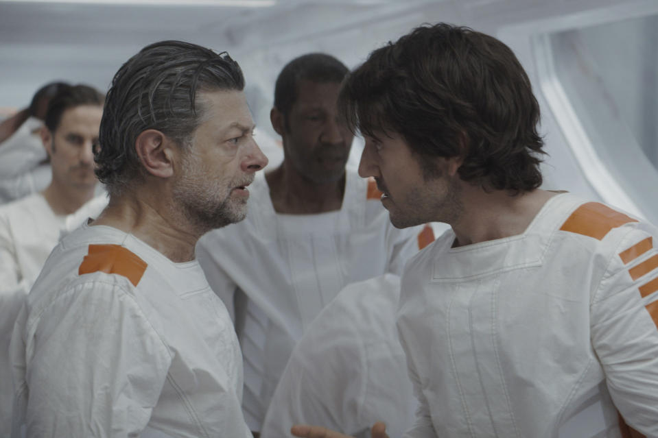 Two men in white prison garb face each other, next to a line of other men; still from "Andor."