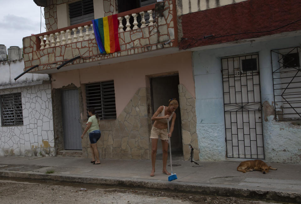 With a pride flag over her balcony, Lisset Diaz Vallejo sweeps the sidewalk in front of her house the afternoon of her wedding day in Santa Clara, Cuba, Friday, Oct. 21, 2022. Vallejo and her partner Liusba Grajales, who have been together for seven years, are of the first to make the decision to get legally married in Cuba following the new Family Code, which opened up everything from equal marriage to surrogate mothers. (AP Photo/Ismael Francisco)