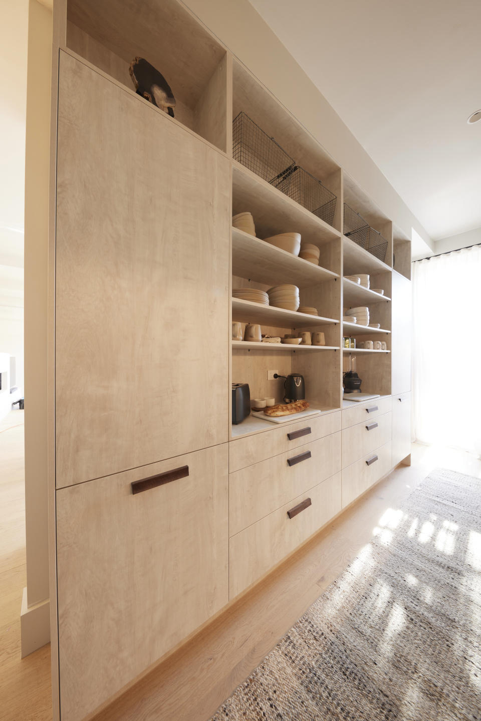 A wall of light timber cupboard and shelves stacked with plates. 