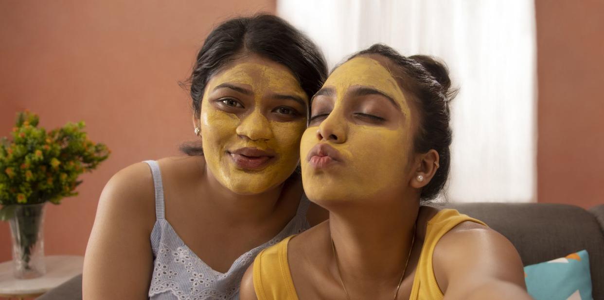 two young women with turmeric face pack taking selfie in living room