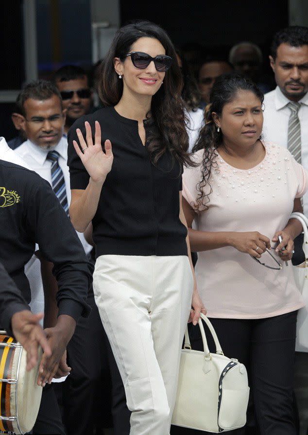 Amal Clooney en pull noir et pantalon blanc.