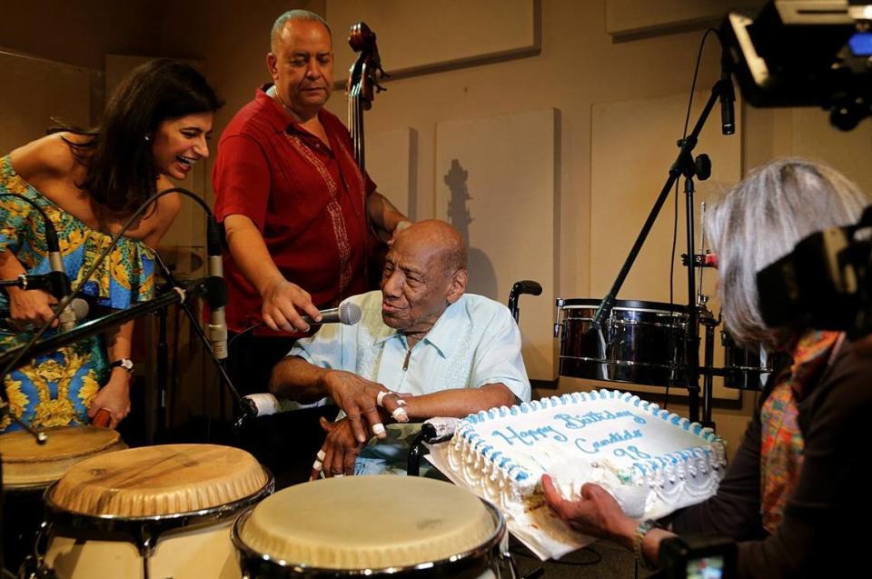 In this file photo from March 16, 2019, Cuban music legend conga and bongo player Candido Camero celebrated his 98th birthday surrounded by friends and fans including, from left to right: Vivian Maria, host of “Cubaneando,” bassist Ramses Colon, and Maggie Pelleyá, general manager at WDNA FM 88.9.