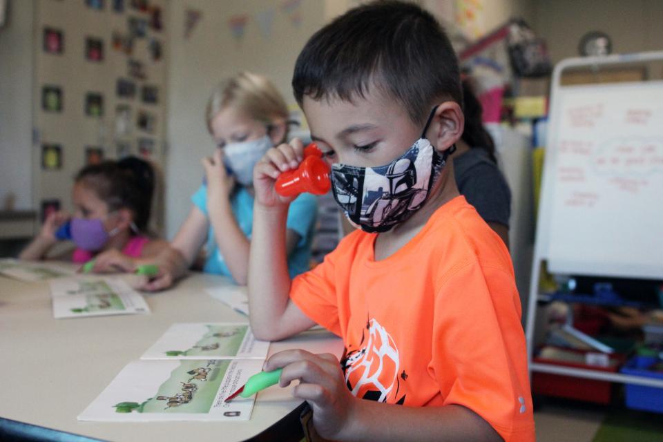 A student uses a whisper phone and a green rubber finger to follow along as he reads during center time.