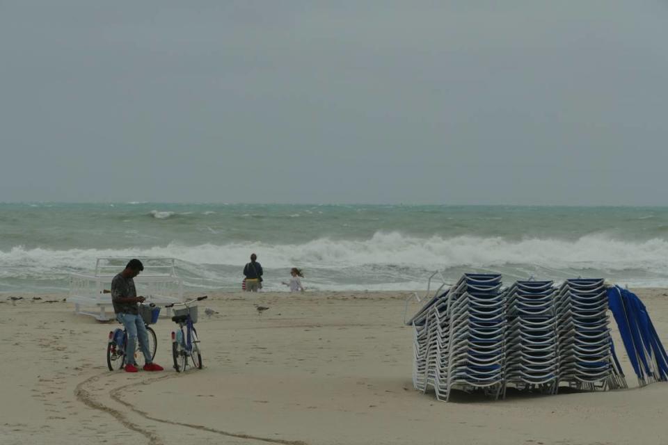 A man waits next to two rented bikes as a woman off-camera takes a closer look at the rowdy waves in Miami Beach, Florida, on Friday, Dec. 15, 2023.