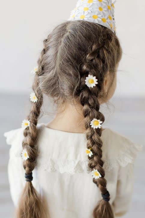 girl with brunette braided hair with white flowers and birthday cone hat with decorative chamomiles on a white wall background