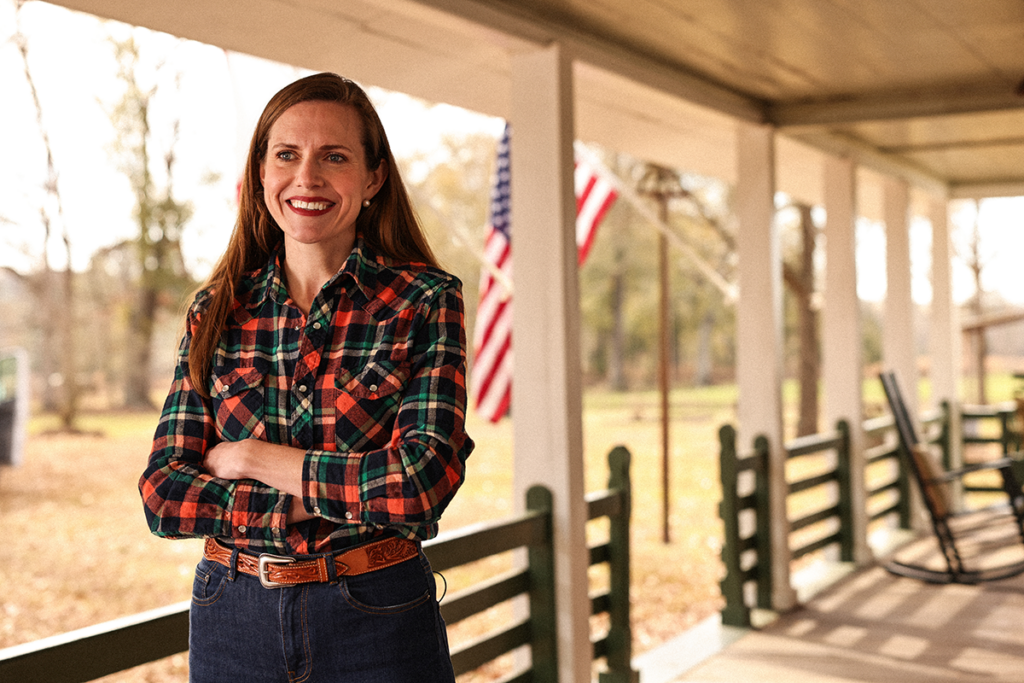 Woman stands on front porch arms crossed, looking past. the camera