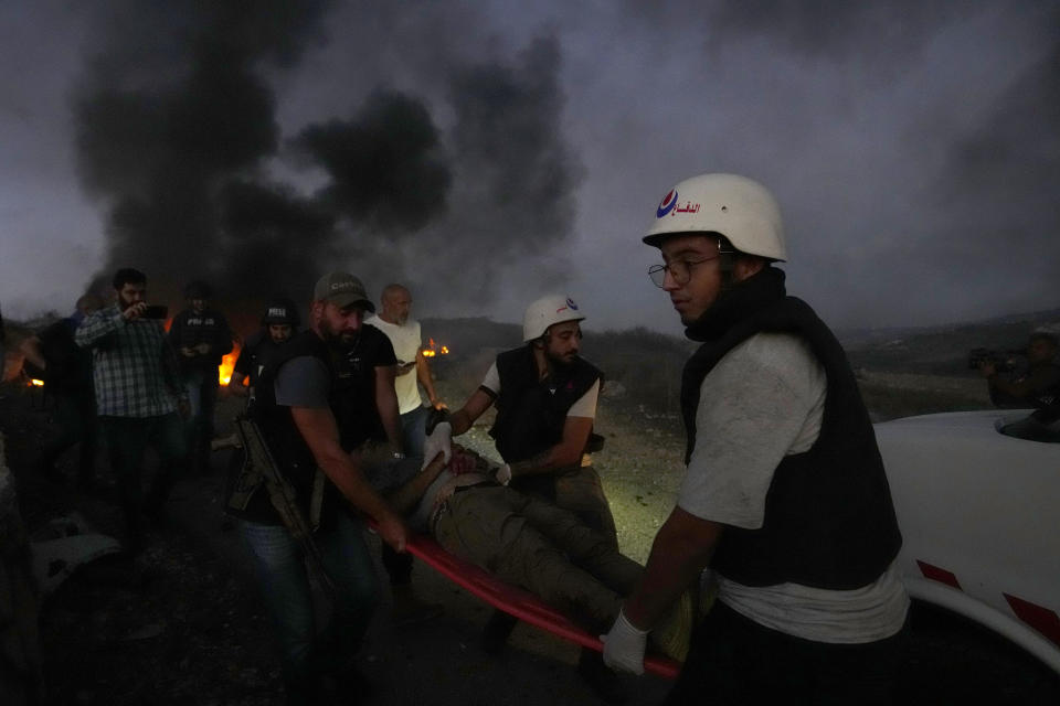 Trabajadores de protección civil y un agente de seguridad libanés cargan a un periodista que resultó herido por la caída de un proyectil israelí en Alma al-Shaab, en el sur de Líbano, el viernes 13 de octubre de 2023. (AP Foto/Hassan Ammar)