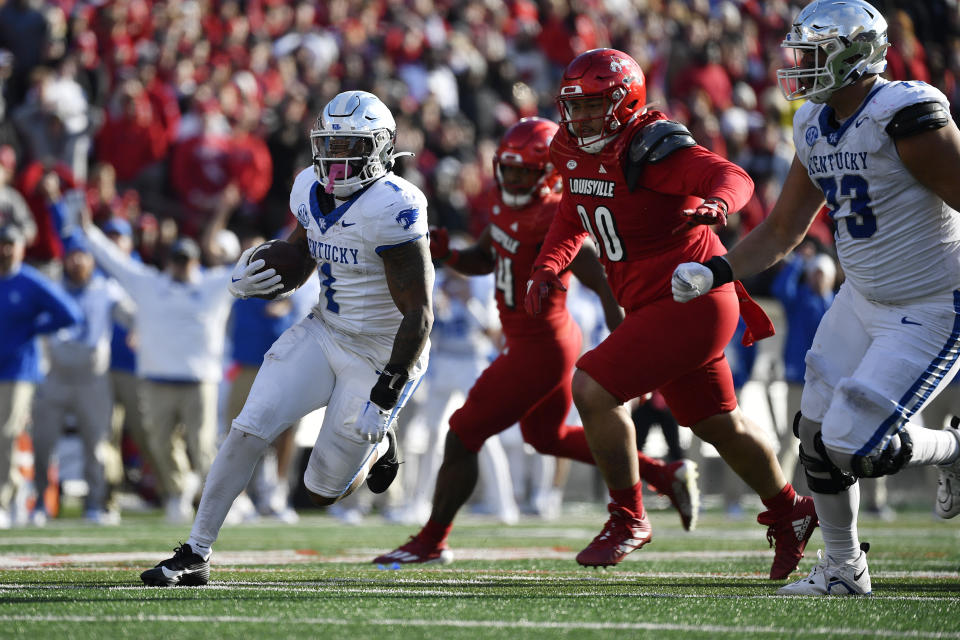 Kentucky running back Ray Davis (1) runs from the defense of Louisville defensive lineman Jermayne Lole (90) during the second half of an NCAA college football game in Louisville, Ky., Saturday, Nov. 25, 2023. Kentucky won 38-31. (AP Photo/Timothy D. Easley)