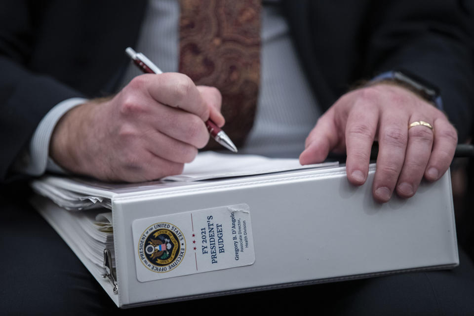 An aide holds a copy of the President's Budget for 2021, as Office of Management and Budget Acting Director Russell Vought testifies during a hearing of the House Budget Committee about President Trump's budget for Fiscal Year 2021, on Capitol Hill, Wednesday, Feb. 12, 2020, in Washington. (AP Photo/Alex Brandon)