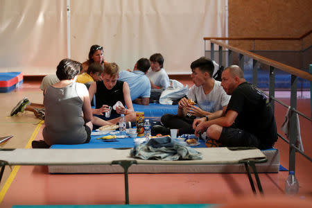 Tourists, who were evacuated due to a forest fire, rest on mats and eat a meal in a gymnasium in Bormes-les-Mimosas, in the Var department, France, July 26, 2017. REUTERS/Jean-Paul Pelissier