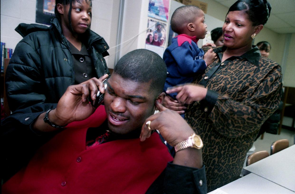 Pearl-Cohn High defensive end John Henderson, front, tries to call Tennessee assistant coach Randy Sanders after signing with the Vols at his high school Feb. 4, 1998. Looking on is his sister, LaTonya, left, and mother, Bridgett, holding his nephew, Tyquez Johnson.